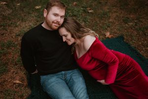 Intimate forest photoshoot featuring a couple relaxing on a dark blanket among trees.