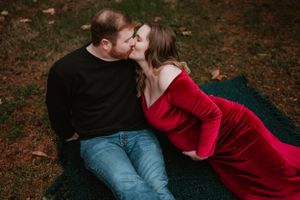 A romantic couple embraces on a blanket in a wooded area during an autumn photo session.