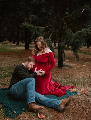 A couple shares an intimate moment while sitting on a blanket surrounded by fallen leaves.