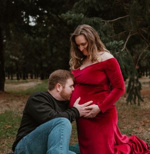 A couple in casual and formal wear poses together on autumn ground in a forest setting.