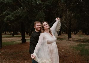 A romantic couple dances together in a wooded area during a maternity session.