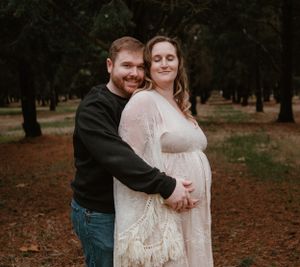 A couple shares a tender moment in a forest setting during their maternity photoshoot.