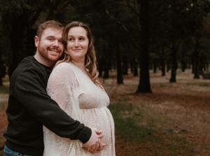 A couple embraces while standing among trees during an outdoor photo session.