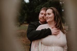A couple shares an intimate moment during their maternity photo session in a wooded setting.