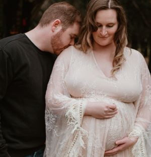 Maternity photoshoot featuring couple in casual and formal wear standing among fallen leaves.