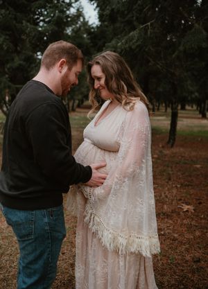 Outdoor maternity photography session showing loving couple in wooded park setting.