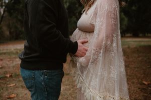 Artistic maternity photos showing couple embracing in autumn forest landscape.