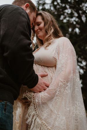 Intimate pregnancy photography with detailed lace dress against autumn forest backdrop.