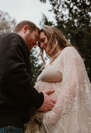 A romantic moment captured in a wooded setting with a flowing lace dress and intimate embrace.