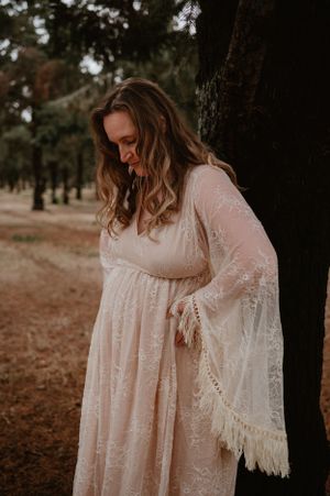Dreamy portrait session showcasing intricate details of a flowing cream-colored lace dress in a forest setting.
