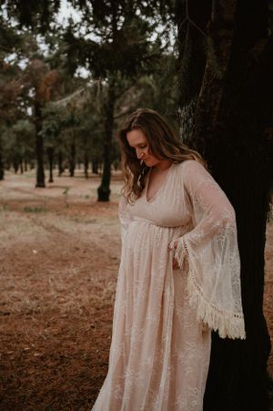Artistic maternity photography in a wooded area featuring a romantic lace gown with bell sleeves.