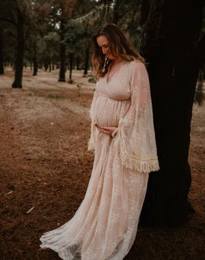 Elegant maternity session in a forest setting with a flowing cream lace dress.