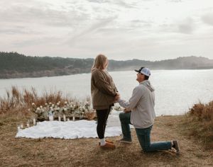 A romantic proposal scene unfolds on a scenic overlook by the water.