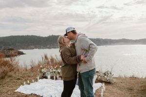 A couple shares a tender moment during a lakeside proposal.