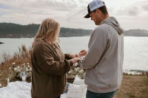 Two people embrace during a surprise proposal on a coastal cliff.