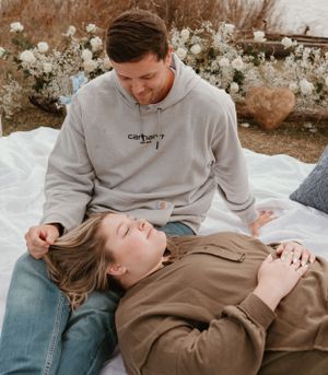 A couple shares intimate moments on a white blanket during their engagement.