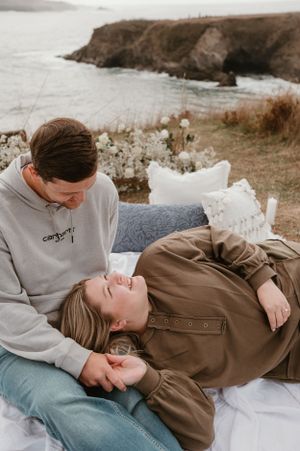 A couple lying on a white blanket outdoors sharing an intimate moment against a natural backdrop.