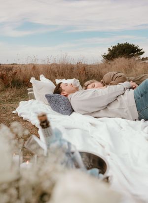 A romantic scene captured from a distance showing a couple resting on a white blanket in nature.