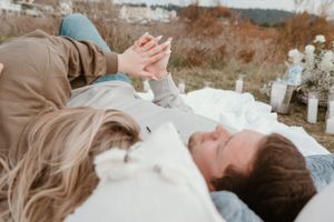An intimate outdoor photoshoot showing a couple on a white blanket near the coastline.