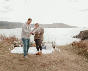 A couple celebrating a special moment on a coastal cliff with ocean views.