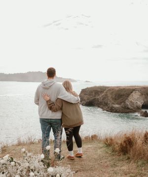 A couple walks along a scenic coastal cliff path with ocean views in the background.