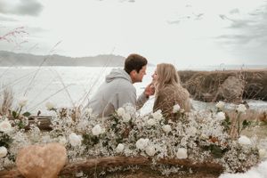 A couple sits together on a blanket overlooking a scenic lake surrounded by rolling hills.