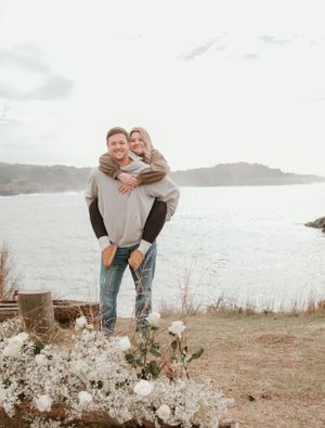 A playful couple shares a joyful moment on a cliff overlooking the ocean.