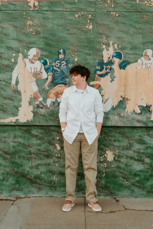 Fashion portraits against distressed green wall wearing white shirt and khaki pants.