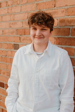 Portrait against red brick wall wearing white button-down shirt in natural lighting.