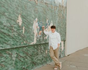 Casual poses against weathered green wall in natural daylight setting.