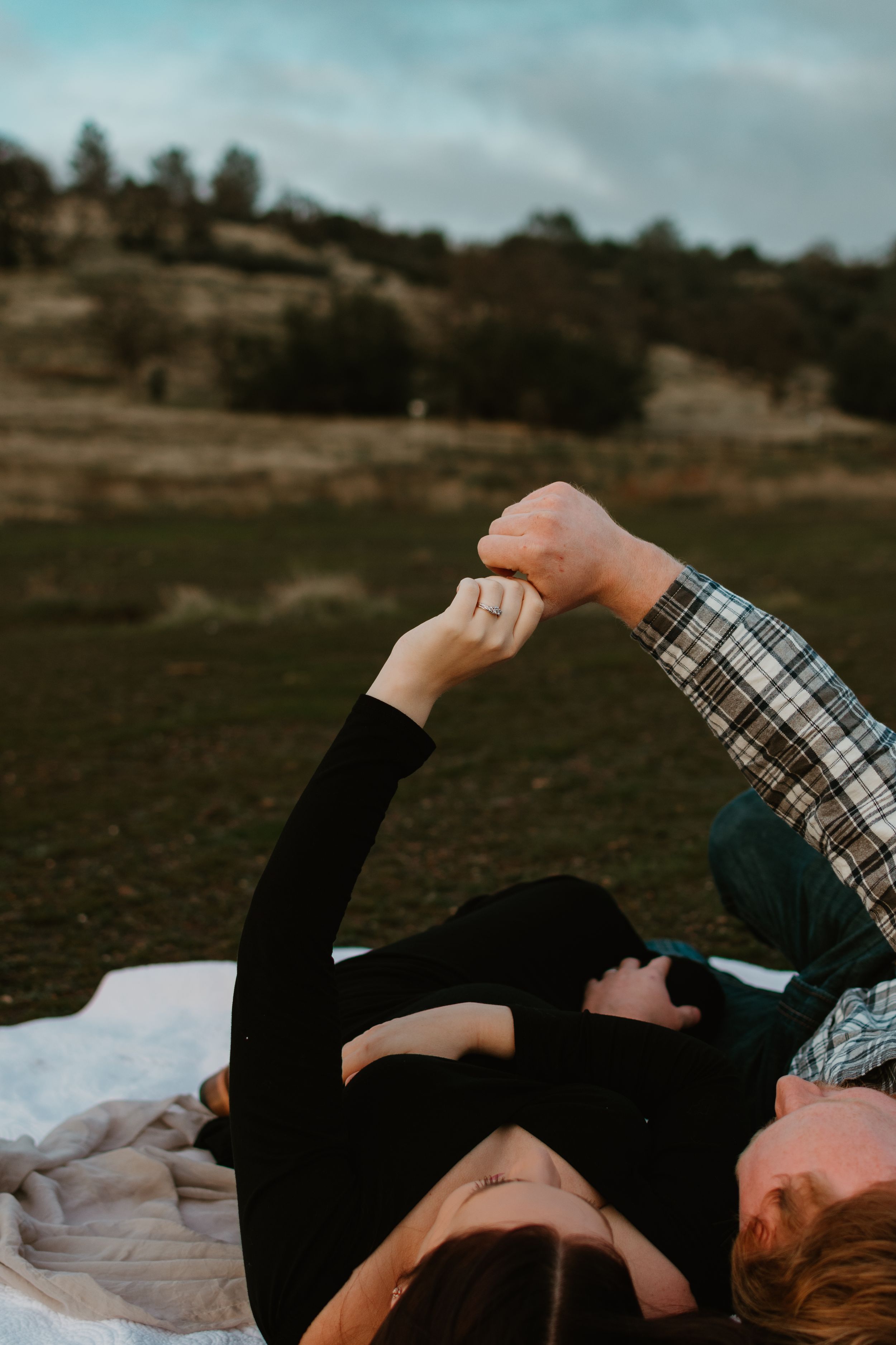 Two people share an intimate moment while lying on a blanket outdoors.