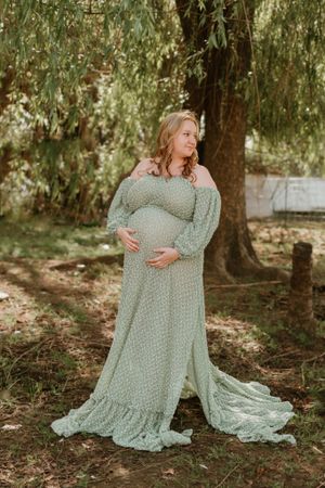 A person in a mint green polka dot dress poses gracefully under willow trees.