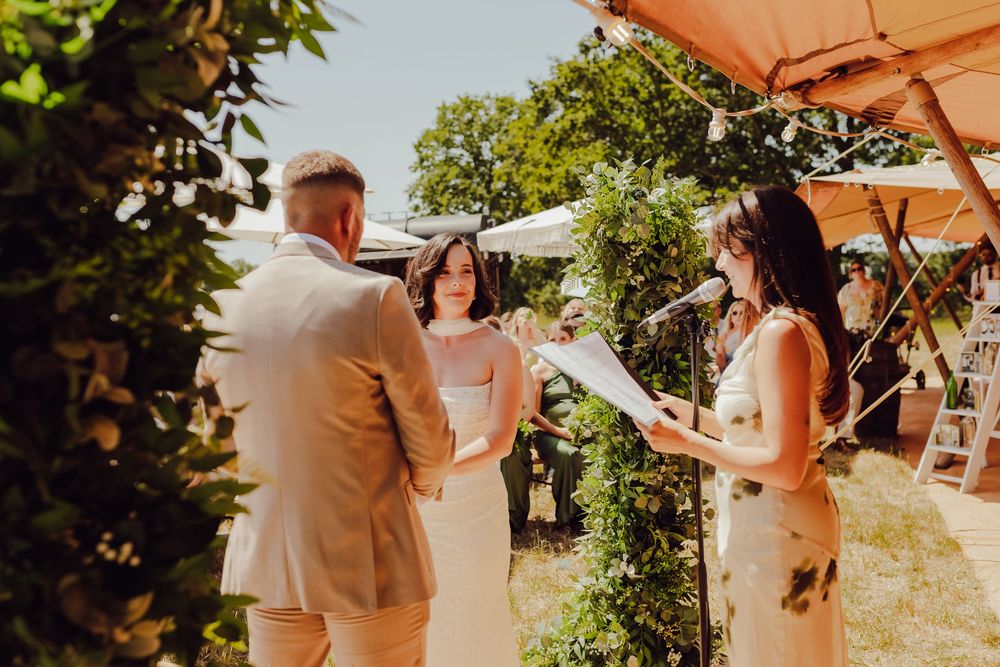 Bride and groom holding hands as they exchange vows in a countryside field.