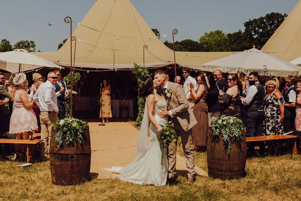 Amy and James sharing a second kiss with their guests celebrating behind them.