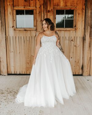 Bride in a strapless lace ball gown wedding dress with floral appliques standing in front of rustic barn doors.