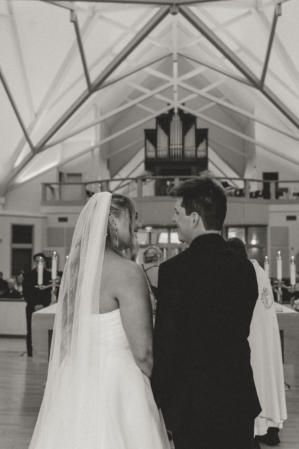 Black and white photo of bride and groom exchanging vows at the altar of a church with pipe organ.