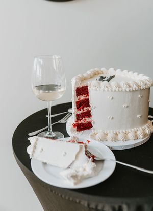 Sliced red velvet wedding cake with white frosting and pearl details next to a glass of white wine.