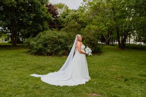 bride in a white gown with a long cathedral veil holding a bouquet in a lush green garden.