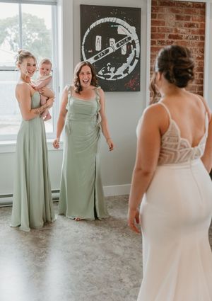 Bridesmaids in sage green gowns reacting with joy during a first look reveal with the bride in white.
