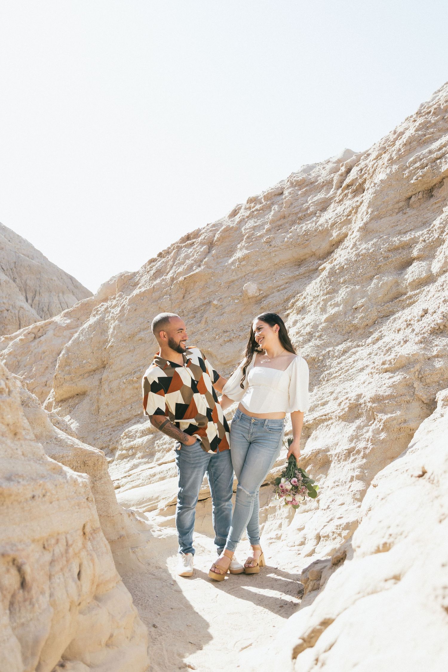 Couple walking together through scenic desert canyon with white limestone rock formations during sunny day.