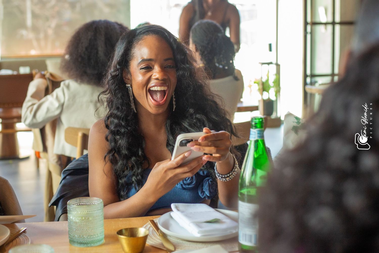 Woman laughing joyfully at restaurant table with drinks and natural lighting.