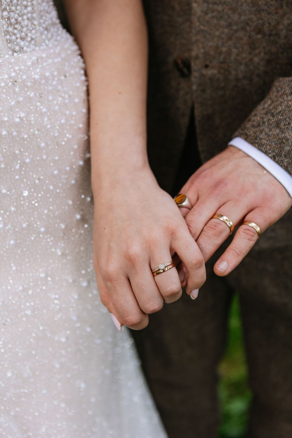 Close-up of bride and groom holding hands and showing their wedding rings against sparkly white gown.