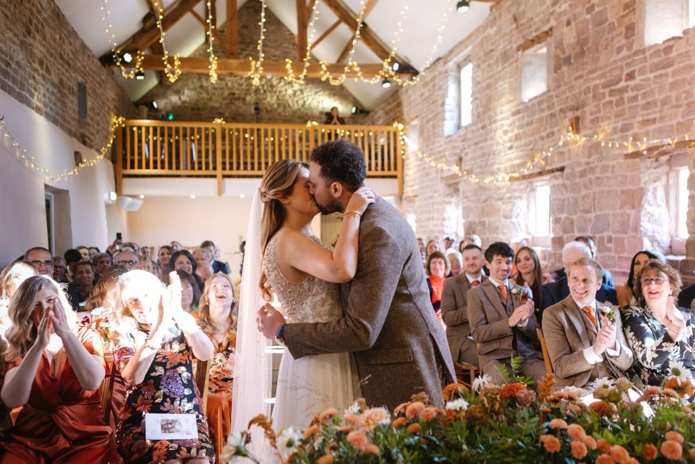 A romantic moment at a rustic barn wedding reception with exposed brick walls and twinkling lights overhead.