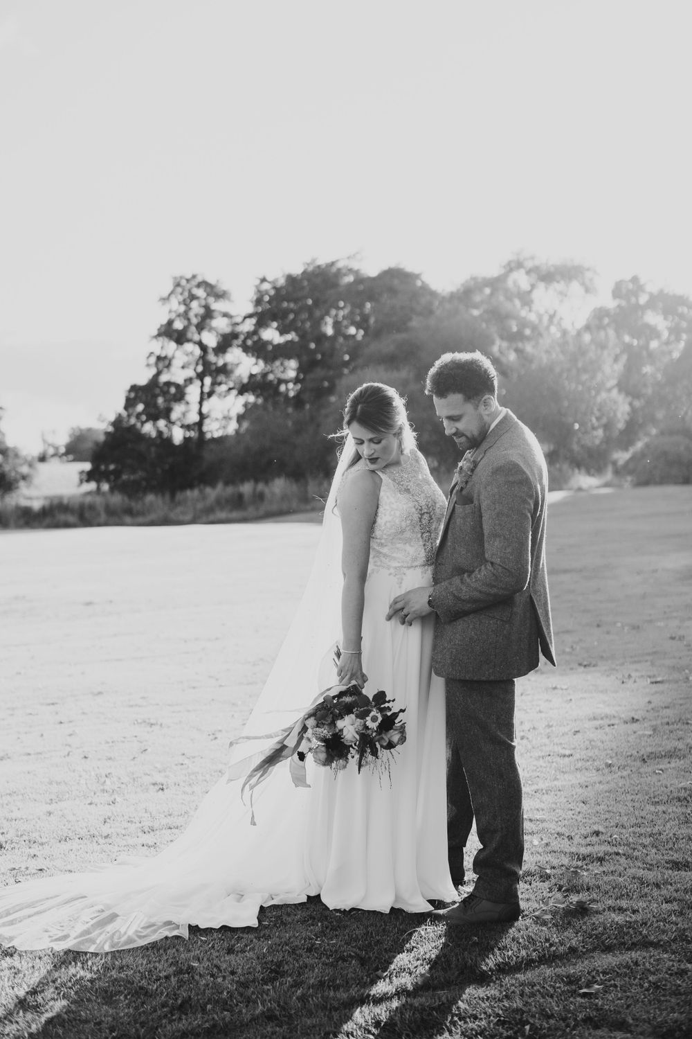 A romantic black and white wedding photo captures a couple sharing a tender moment outdoors at sunset.
