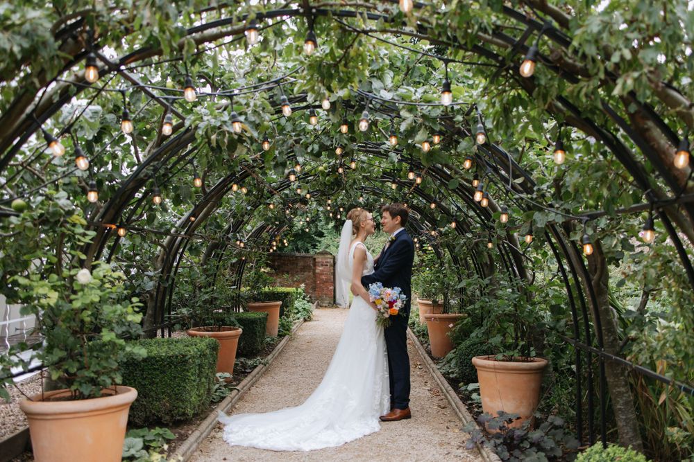 A romantic garden arch tunnel covered in greenery and string lights creates an intimate wedding backdrop.