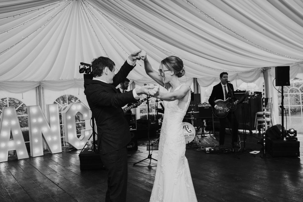 Couple dances together at a wedding reception in a white tent while the band performs in the background.