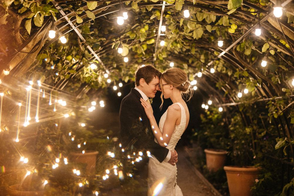 Romantic evening scene with couple dancing under glowing string lights and leafy canopy at outdoor garden venue.