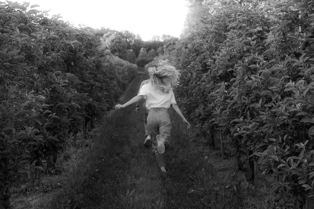A person leaps joyfully down a garden path between tall hedgerows in a black and white photograph.