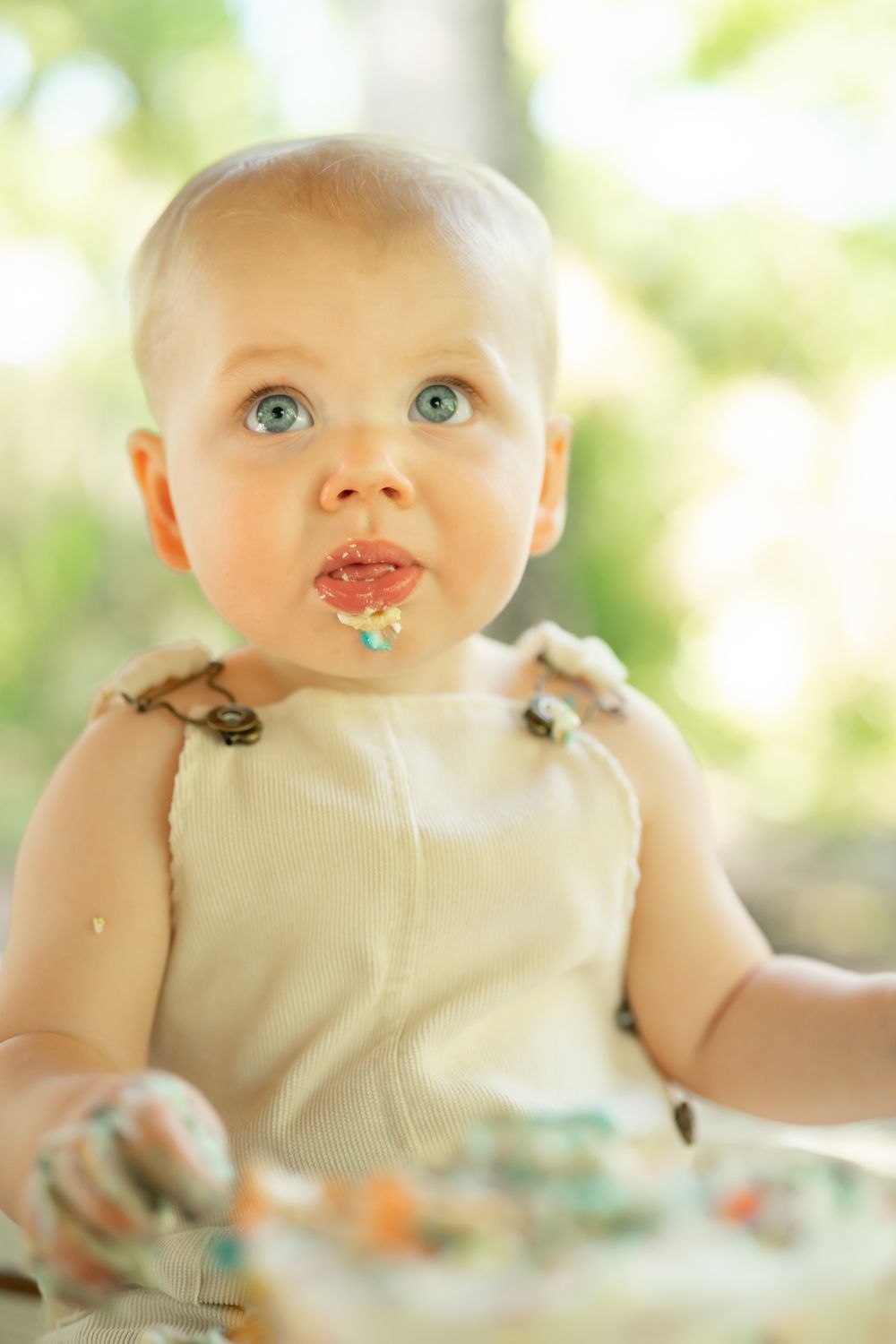 Baby sitting in a high chair during a messy feeding session with food smeared on their face and bib.