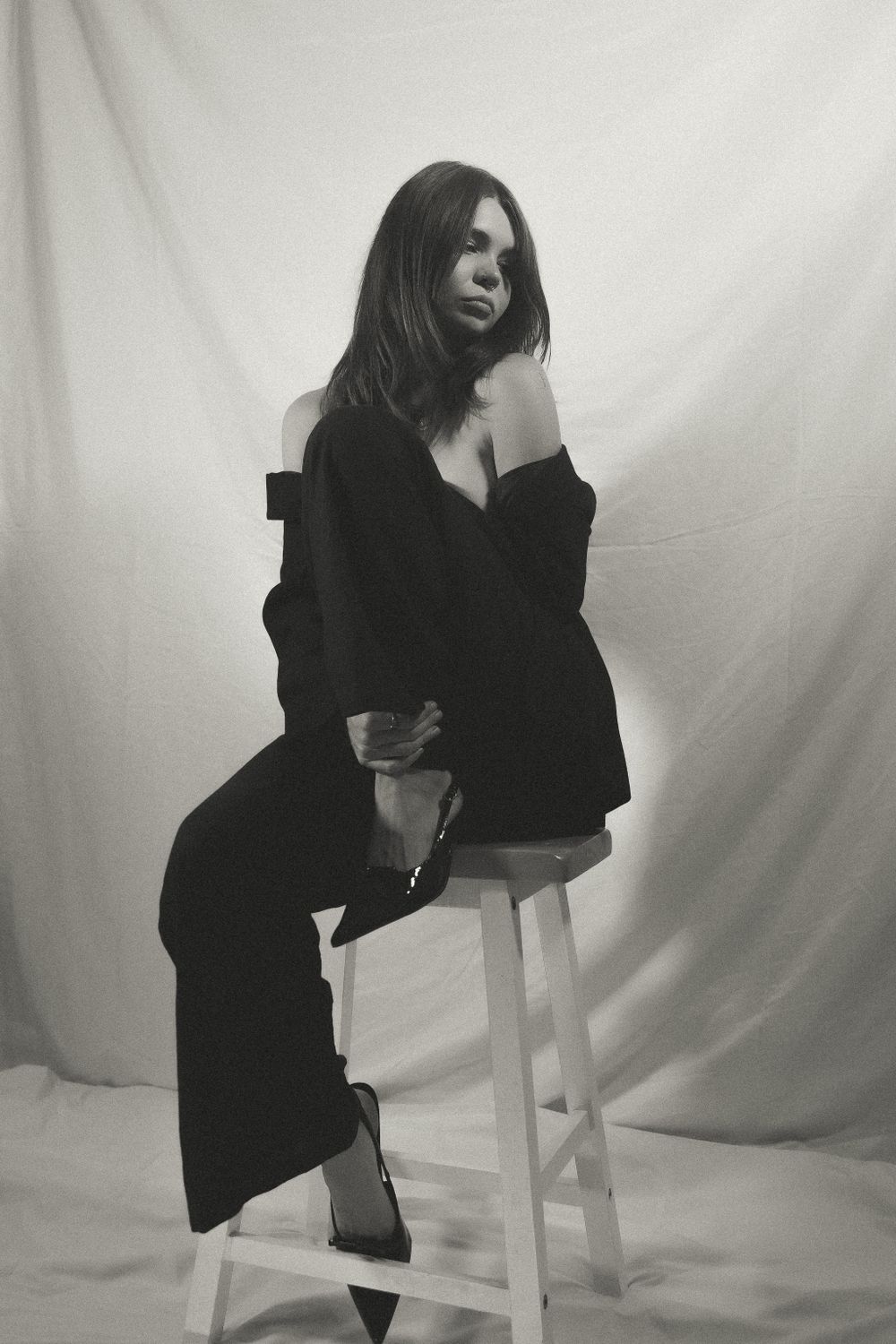 Black and white portrait series of figure posing on wooden stool against white backdrop.